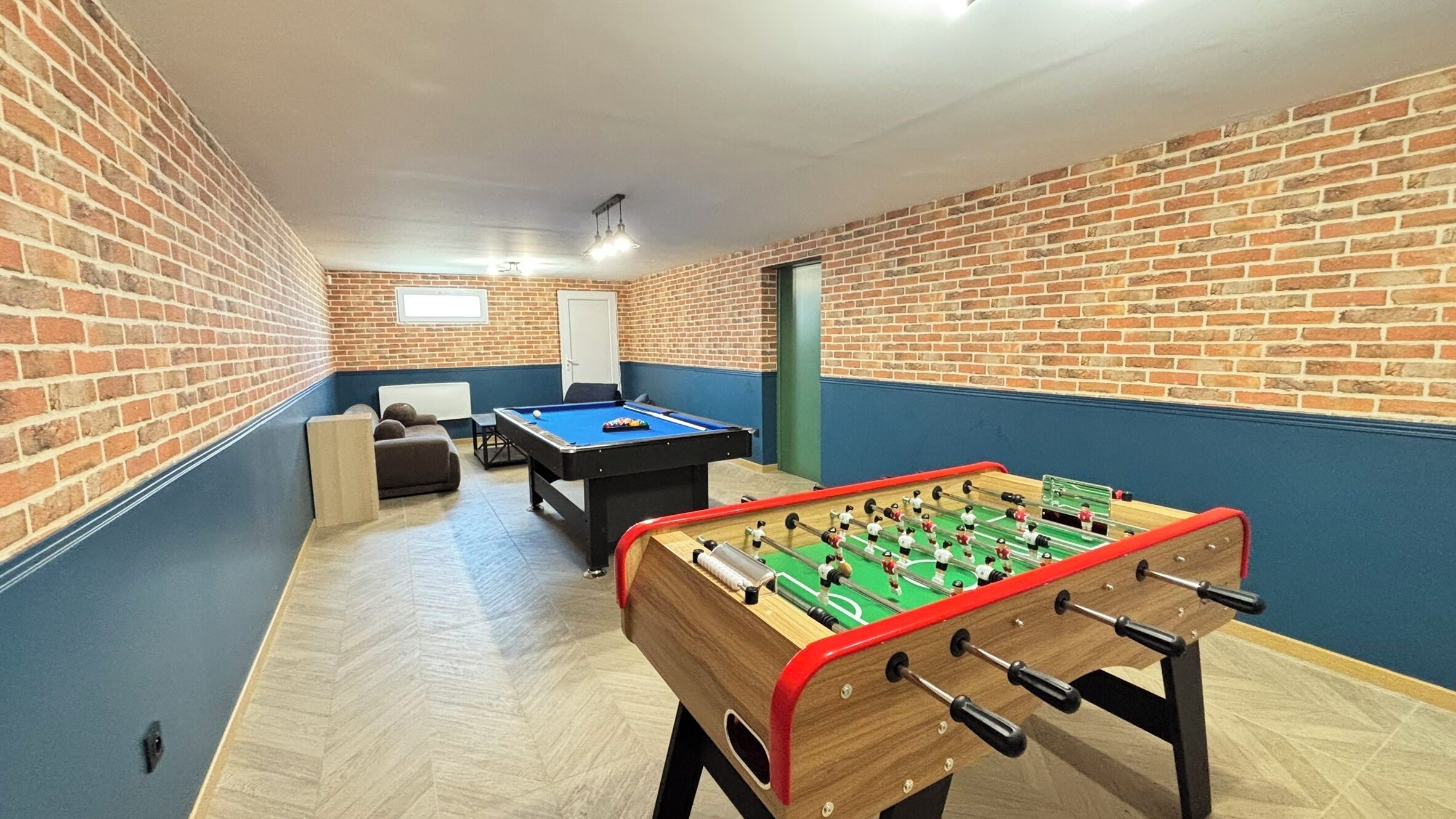 Een kamer met een tafelvoetbaltafel, een pooltafel en een bank.