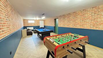 Een kamer met een tafelvoetbaltafel, een pooltafel en een bank.