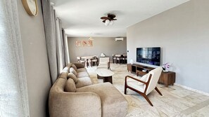 A modern living room with a sofa, coffee table, TV, and a dining area.