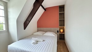 A bedroom with a sloped ceiling, a bed with striped bedding, a bedside lamp, and a wooden shelf unit. - Villa César - Private padel court, heated pool from March through November. (Bransles)