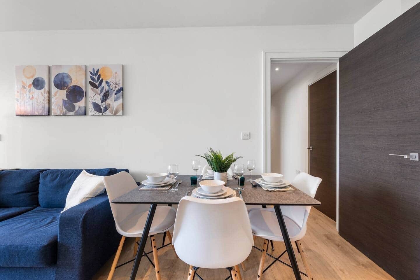 A dining area with a table set for four, white chairs, and a dark wooden door.