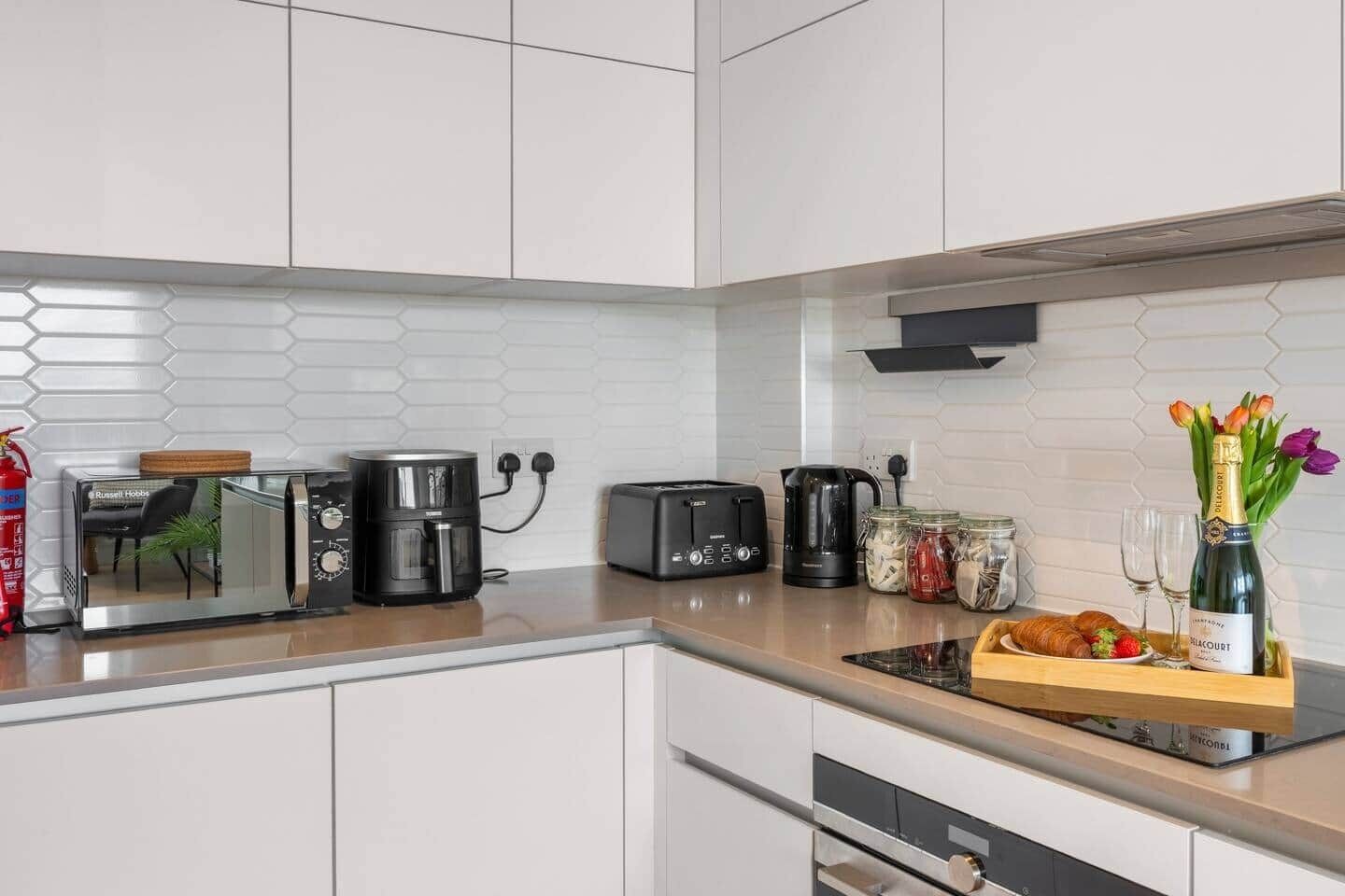 A modern kitchen with a microwave, coffee maker, toaster, and a vase with flowers on the counter.