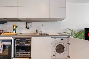 A modern kitchen with white cabinets, a dishwasher, and a built-in washing machine. - Boston House, Wembley HA9 (London)