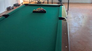 A pool table with balls, a pool cue, and a table tennis table in a room with a view of a body of water through a large arched window. - 2-bedroom apartment in Sunny Freeport with cool AC. Across from Beach. (Freeport)