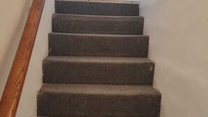 A carpeted staircase with a wooden handrail leading to an interior space. - 2-bedroom apartment in Sunny Freeport with cool AC. Across from Beach. (Freeport)