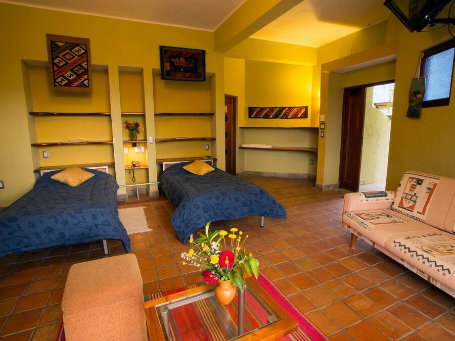 A room with two beds, a sofa, a small table with a vase, and shelves with decorative items.