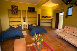 A room with two beds, a sofa, a small table with a vase, and shelves with decorative items.
