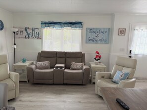 Ein Wohnzimmer mit einem beigen Sofa, zwei Beistelltischen, einem Couchtisch und einem Fenster mit Jalousien.
