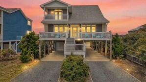 A two-story house with a balcony, a covered porch, and a gravel driveway. - Mischief Managed NC-  Marsh and Beach views!  Private Pool, Pet Friendly (Oak Island)