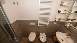 Ein Badezimmer mit zwei Toiletten, einem Bidet, einem Waschbecken, einem Spiegel und einem Handtuchhalter.