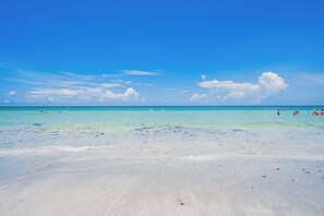 Una playa con agua turquesa cristalina, arena blanca y algunas personas a lo lejos.