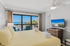 A hotel room with a bed, a television, a view of the beach, and a balcony with chairs. - Gulf Front Condo - Sand Castle North 304 (Indian Rocks Beach)