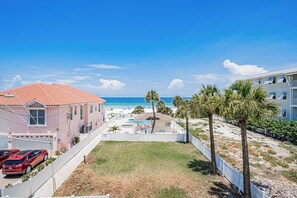 A beachfront property with a swimming pool, a red car parked in the driveway, and a view of the ocean. - Gulf Front Condo - Sand Castle North 304 (Indian Rocks Beach)