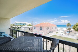 A balcony with wicker furniture overlooking a beach with houses and a clear sky. - Gulf Front Condo - Sand Castle North 304 (Indian Rocks Beach)