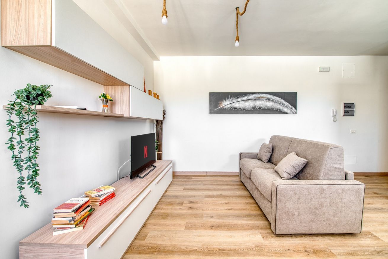 Ein modernes Wohnzimmer mit Flachbildfernseher, einer Couch, Holzboden und einem Wandregal mit Büchern und einer Pflanze.