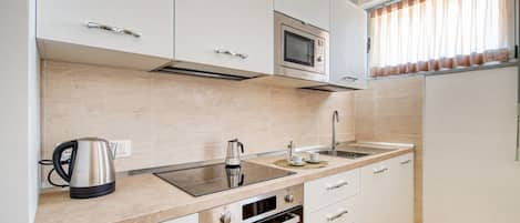 A modern kitchen with white cabinets, a stainless steel kettle, a microwave, and a built-in oven.