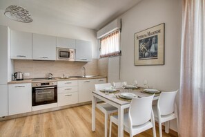 Una cocina moderna con armarios blancos, microondas, horno y una mesa de comedor preparada para cuatro.
