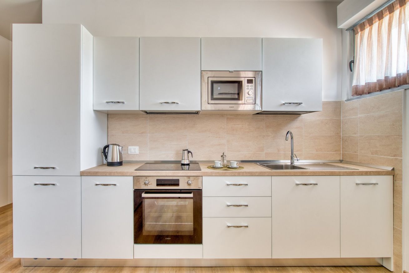 A modern kitchen with white cabinets, a built-in microwave, a stove, and a sink.