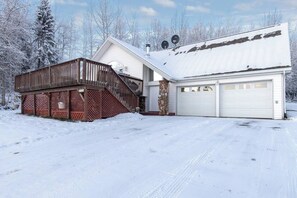 A two-story house with a wooden deck, a garage, and a snow-covered landscape.