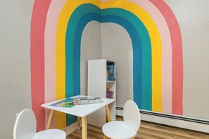A room with a white table and chairs, a bookshelf, and a wall painted with a rainbow design.