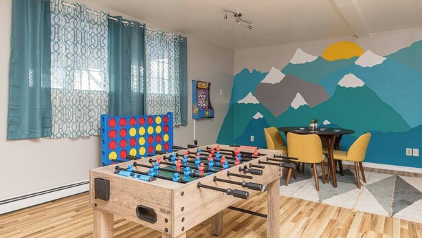 Una habitació amb taula de futbolí, taula amb caires i un mural a la paret.