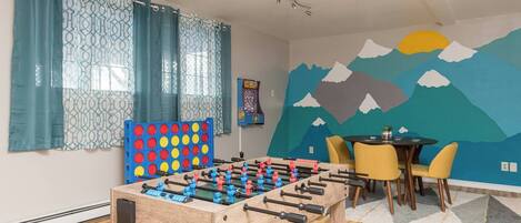Une pièce comprenant une table de baby-foot, une table avec des chaises et une fresque murale.