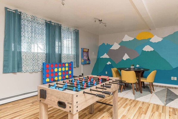 A room with a foosball table, a table with chairs, and a wall mural.