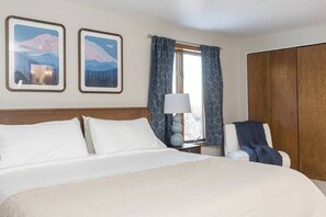 Een hotelkamer met een groot bed, een nachtkastje met een lamp, een kledingkast en twee wanddecoraties.