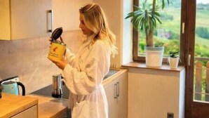 A person in a white robe in a kitchen with a sign reading 'ESPRESSO' and a view of greenery outside.