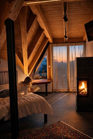Ein gemütliches Zimmer mit schrägen Wänden, einem Kamin, einem Bett und einem großen Fenster.