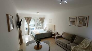 Habitación de hotel con cama, sofá, mesa con sillas, una planta pequeña y obras de arte en las paredes.