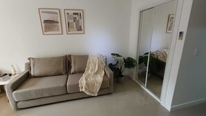 A living room with a beige sofa, a small table, a potted plant, and a sliding door. - Beautiful studio apartment in Green Park II, Solanas, Punta del Este (Maldonado)