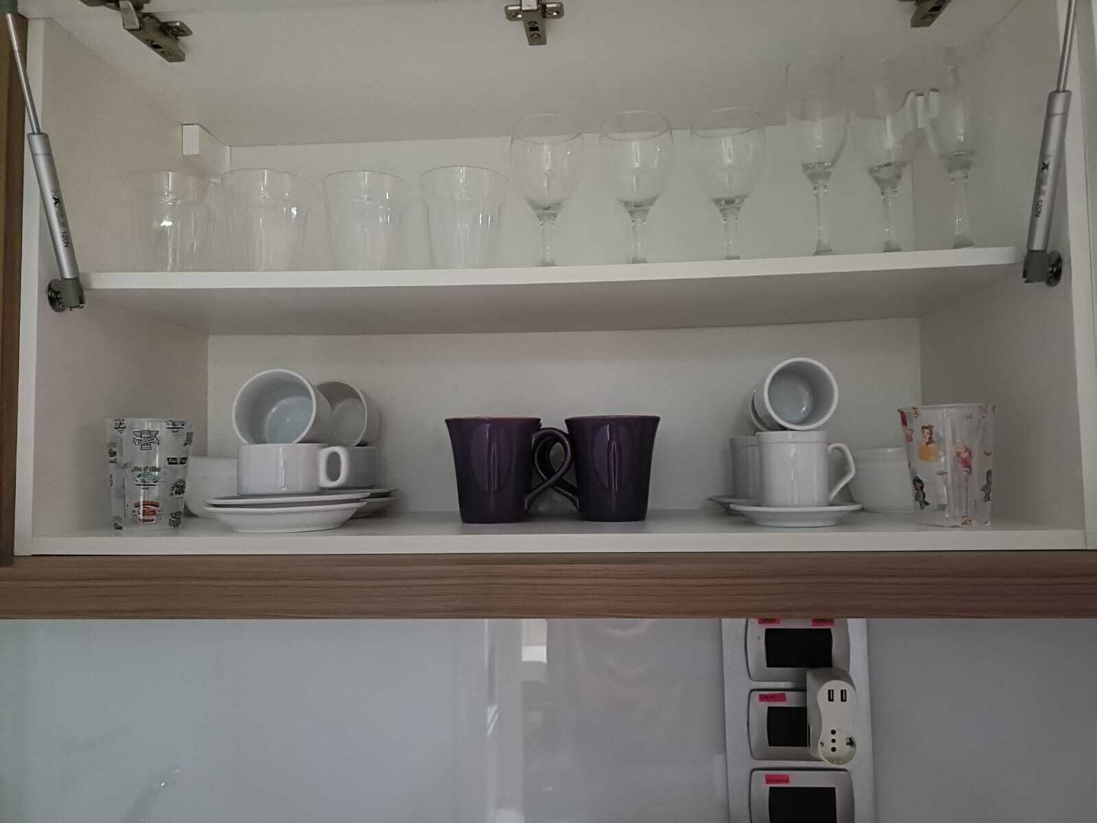 A kitchen shelf with glassware, plates, and cups.
