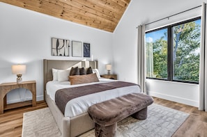 A bedroom with a bed, bedside lamps, a window with a view of trees, and a wooden ceiling. - Luxury Roof Top Cabin! Splashing Views! Pool! Hot Tub! Gaming Simulator! (Sevierville)