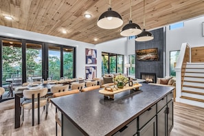 A modern kitchen with a large island, dining area with chairs and tables, and a fireplace. - Luxury Roof Top Cabin! Splashing Views! Pool! Hot Tub! Gaming Simulator! (Sevierville)