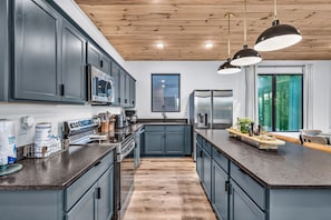 A modern kitchen with dark cabinetry, stainless steel appliances, and a central island. - Luxury Roof Top Cabin! Splashing Views! Pool! Hot Tub! Gaming Simulator! (Sevierville)