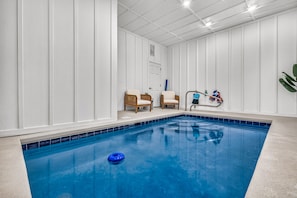 En inomhuspool med en blå vattenfontän, två fåtöljer i rotting och en blå leksak för användning i vattnet.