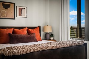 Un lit bien fait, recouvert d’une couverture à motifs, avec une lampe et deux œuvres d’art encadrées accrochées au mur.