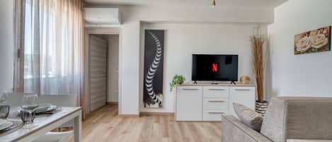 Una sala de estar moderna con una televisión de pantalla plana, un sofá, una mesa de comedor con sillas y una cocina con un mueble para televisión.