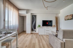 Ein modernes Wohnzimmer mit Flachbildfernseher, einer Couch, einem Esstisch mit Stühlen und einer Küchenzeile mit einem TV-Schrank.