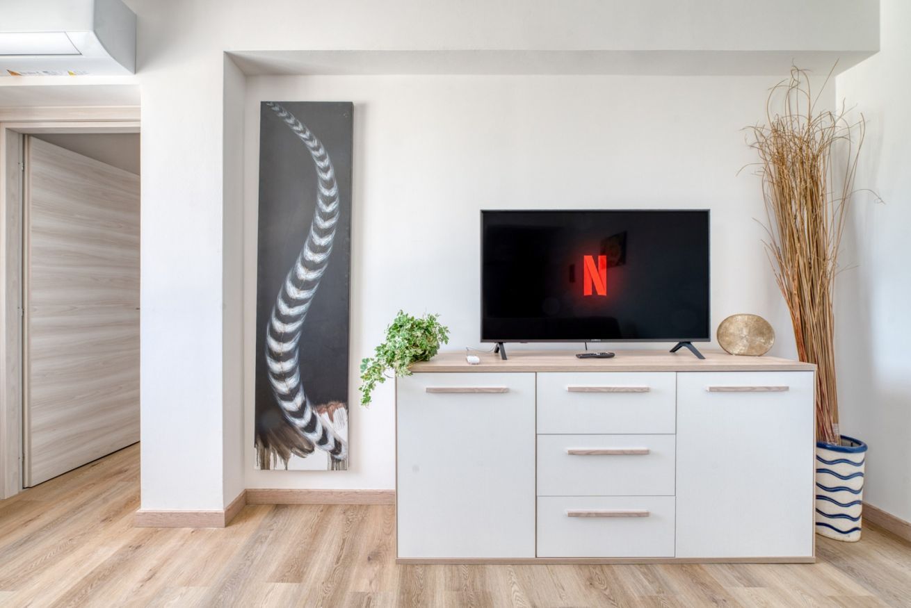 A modern living room with a flat-screen TV, a white cabinet, and a large abstract painting.
