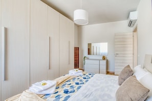 Quarto com cama, guarda-roupa, penteadeira e espelho, além de ar condicionado.