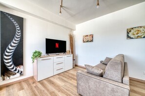 Uma sala de estar moderna com uma TV de tela plana, um sofá, uma planta e obras de arte nas paredes.