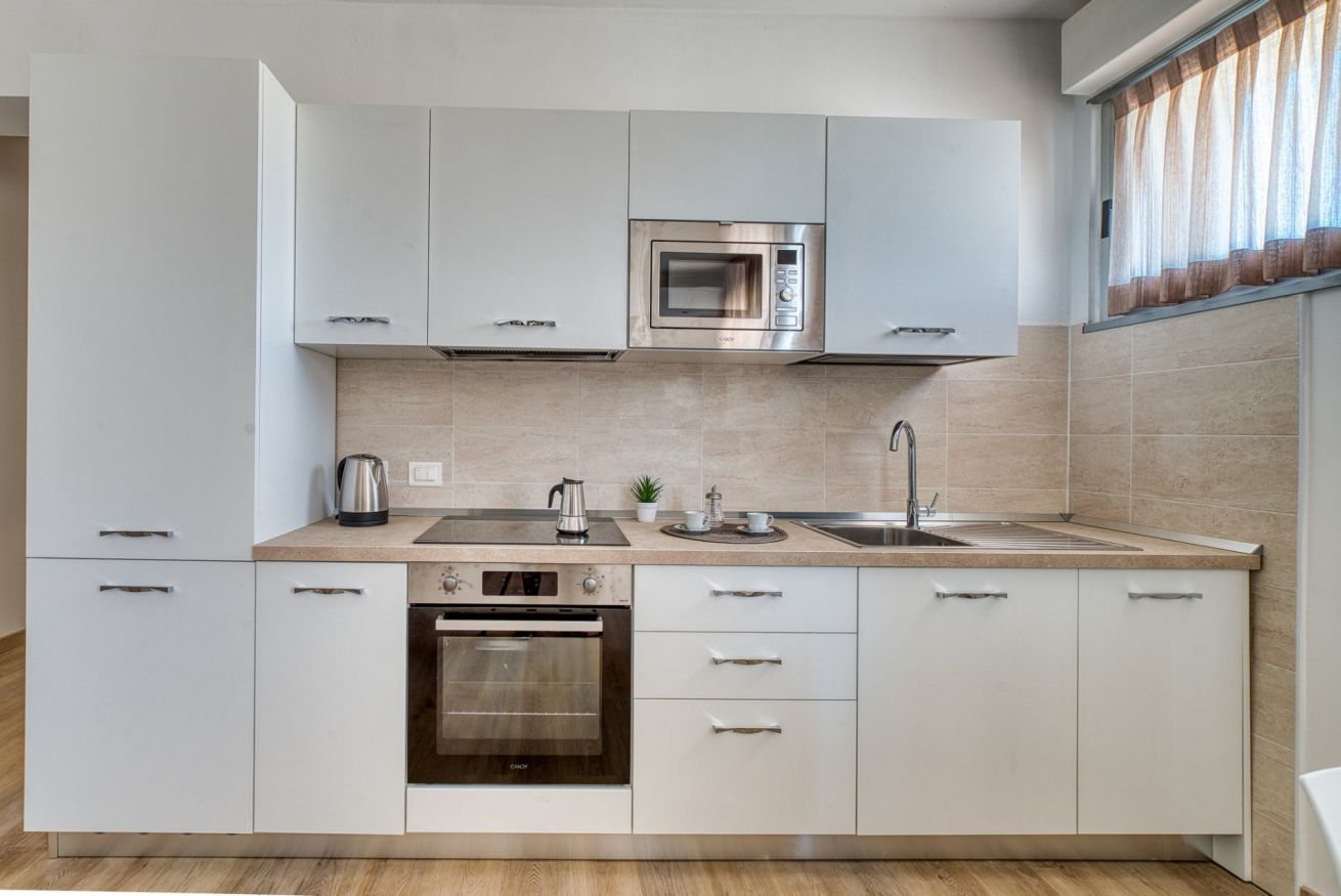 A modern kitchen with white cabinets, a built-in oven, a microwave, and a sink.