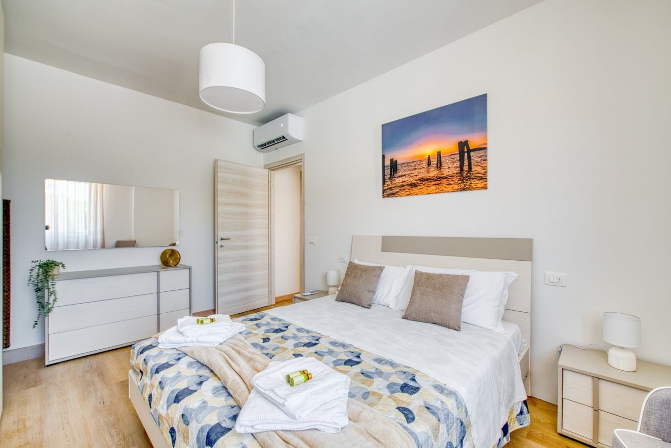 Une chambre à coucher avec un lit, des tables de chevet, un miroir et un tableau représentant un coucher de soleil.