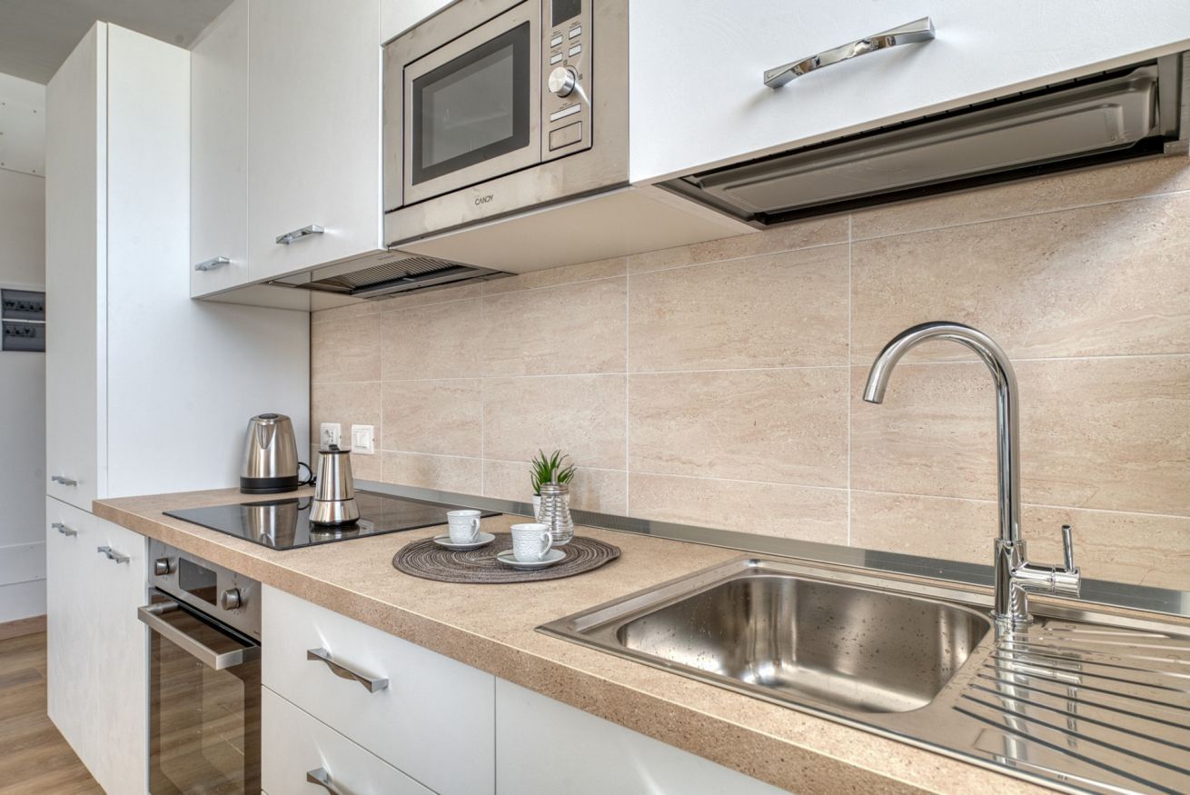 Een moderne keuken met roestvrijstalen apparatuur, een spoelbak en een aanrecht met waterkoker en kopjes.