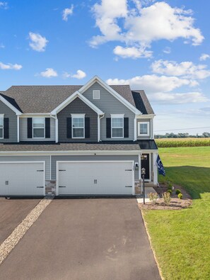 A two-story house with a garage, a stone foundation, and a flag. - New 3BR/3.5BA end unit townhouse under 3.5 mi from Beaver Stadium-full basement (State College)