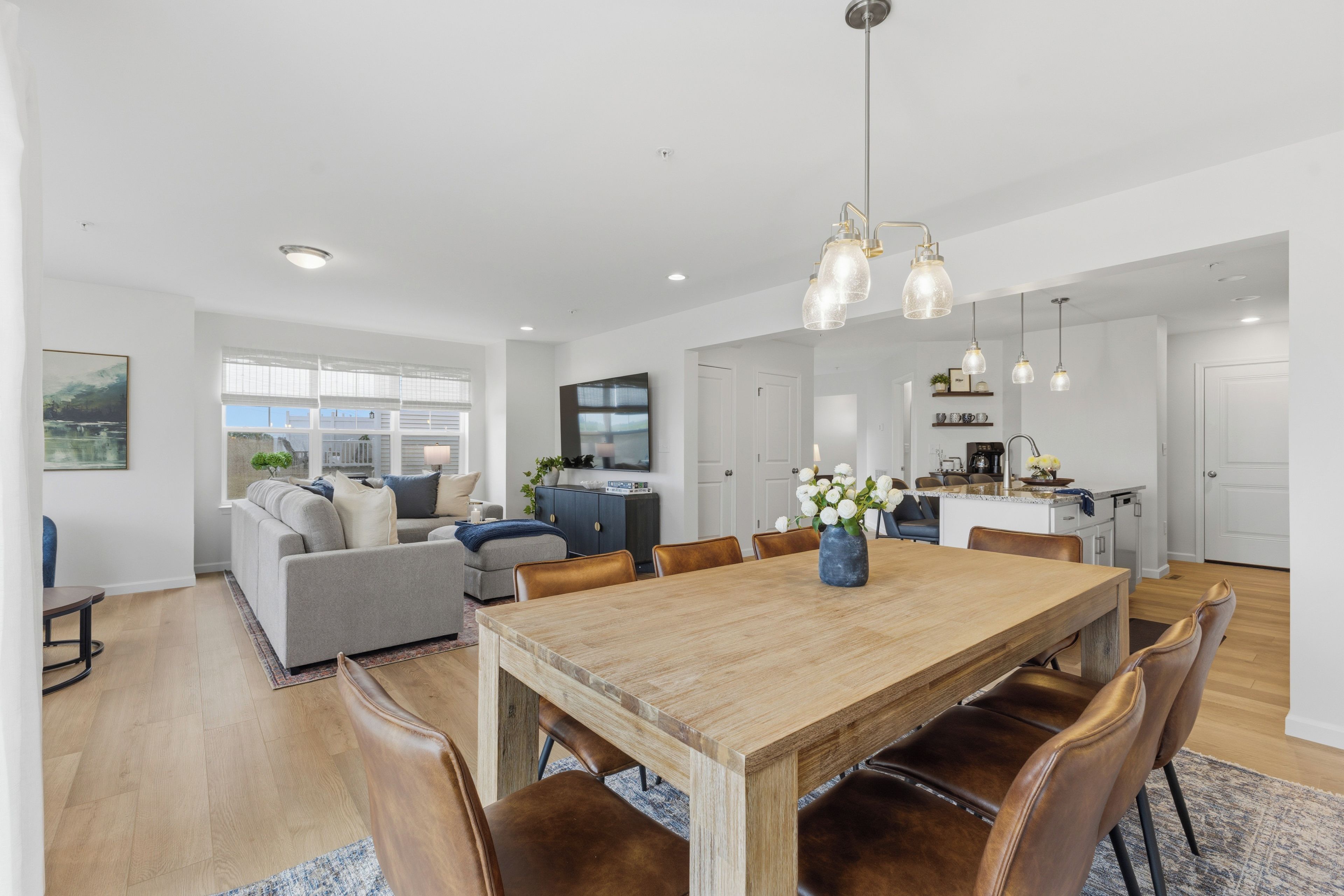 Een ruime woonkamer met een houten eettafel, lederen fauteuils, een bank en een keuken op de achtergrond.