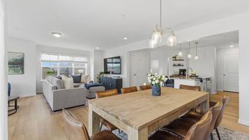 Een ruime woonkamer met een houten eettafel, lederen fauteuils, een bank en een keuken op de achtergrond.