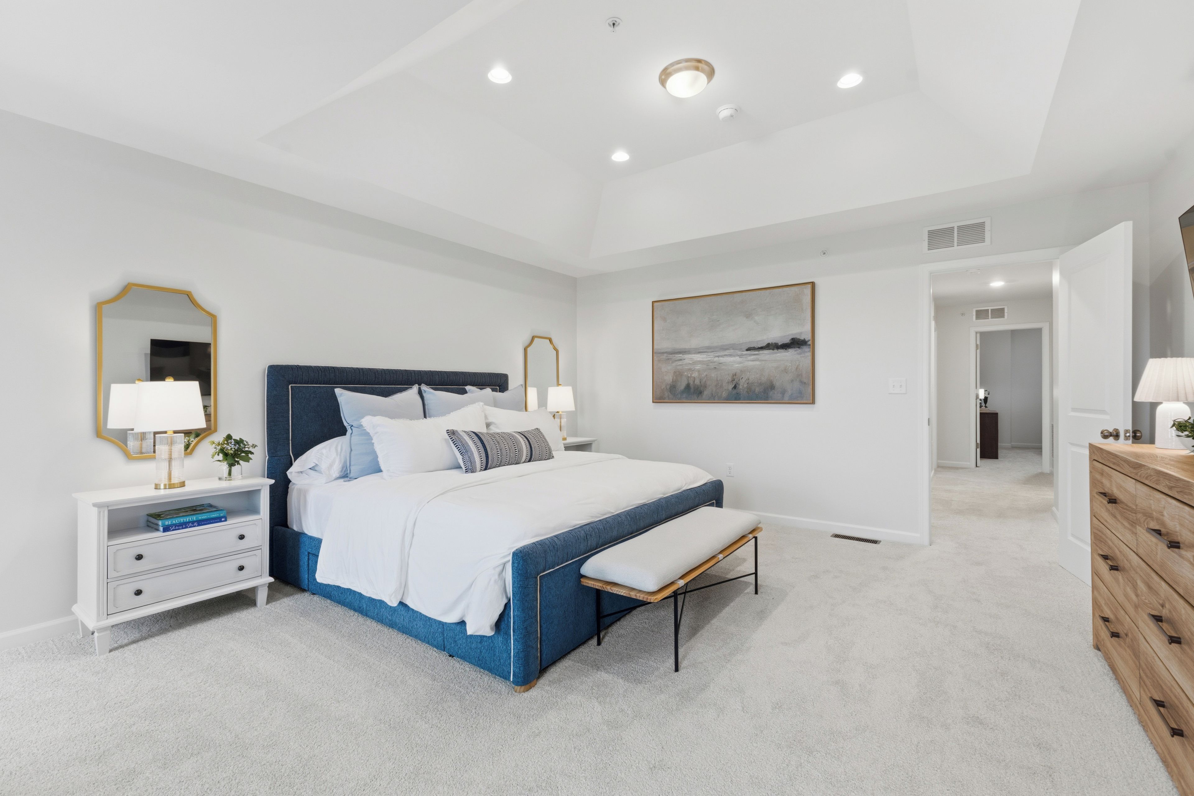 A bedroom with a large bed, bedside tables, a dresser, and a painting on the wall.